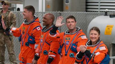 Artemis II astronauts wave while wearing their suits
