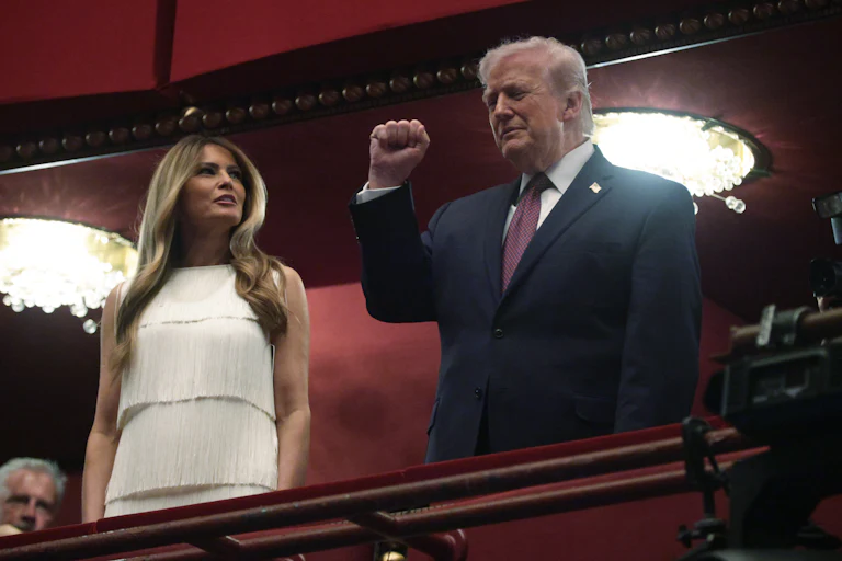 Donald Trump raises his fist while standing next to Melania Trump in a balcony at the Kennedy Center