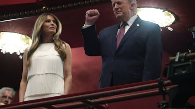 Donald Trump raises his fist while standing next to Melania Trump in a balcony at the Kennedy Center