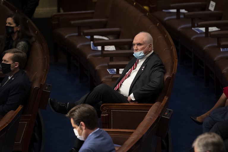 Representative Mike Kelly wears a mask and is seated in the House chamber. One other person is seated two chairs down; other chairs around him are empty.