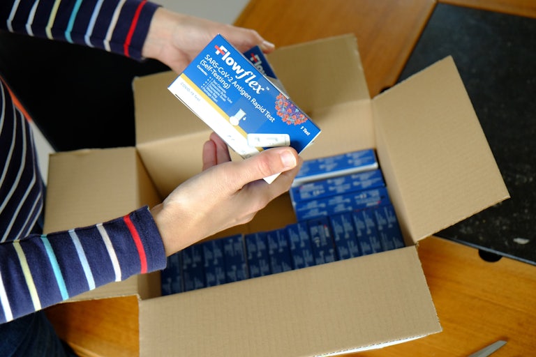 A woman unboxes a box of COVID-19 rapid antigen tests.