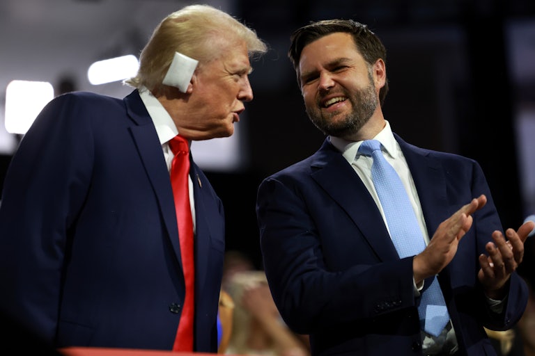 Donald Trump with a cushion on his right ear leans over to speak to J.D. Vance, who is smiling and clapping. Both are at the RNC.