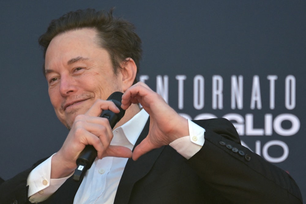Elon Musk makes a heart with his hands while holding a microphone.