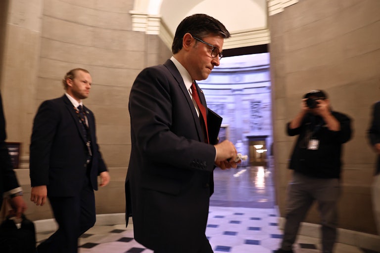 Mike Johnson walking through the Capitol. A photographer in the background takes a photo of him.