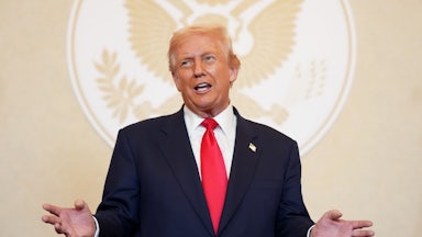 Donald Trump speaks in front of a presidential seal silhouette.