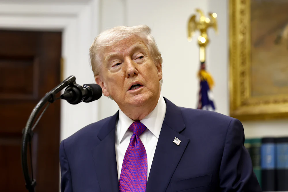 Donald Trump speaks into a microphone while wearing a purple tie and looking to the right.