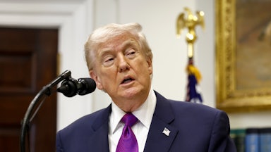 Donald Trump speaks into a microphone while wearing a purple tie and looking to the right.