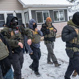 Masked federal agents walk outside a home in Minneapolis, the yard blanketed with snow.