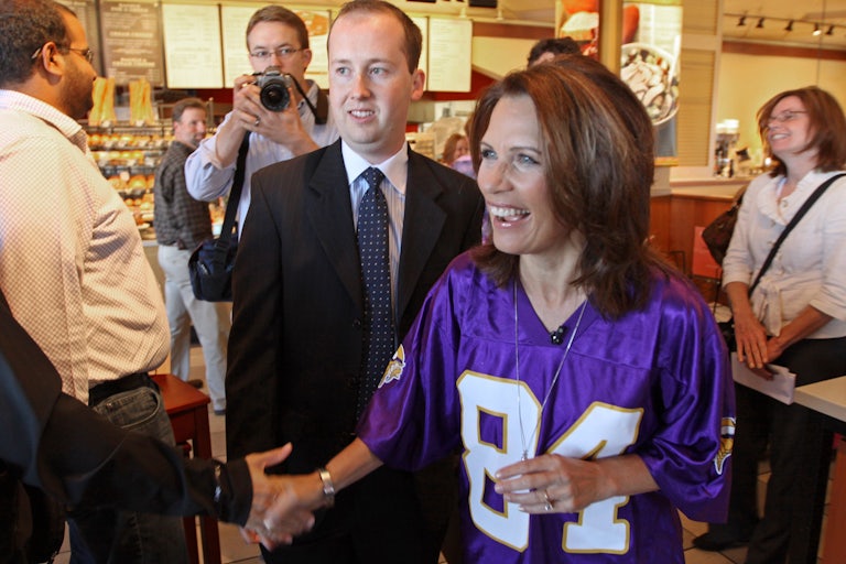 A congresswoman wears a Randy Moss Minnesota Vikings jersey. Sergio Gor, the subject this story and then a young aide, awkwardly stands behind her. He is already bald.