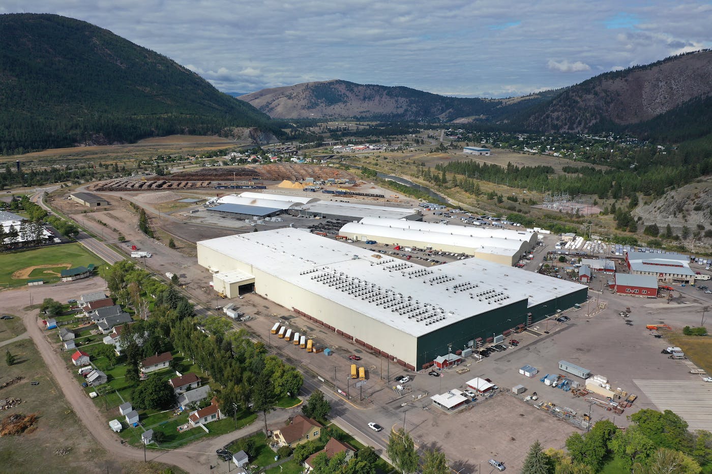 An industrial park sits amid mountains, next to a row of houses.