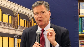 Former FBI Director James Comey gestures with one hand and speaks into a microphone during an event