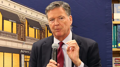 Former FBI Director James Comey gestures with one hand and speaks into a microphone during an event