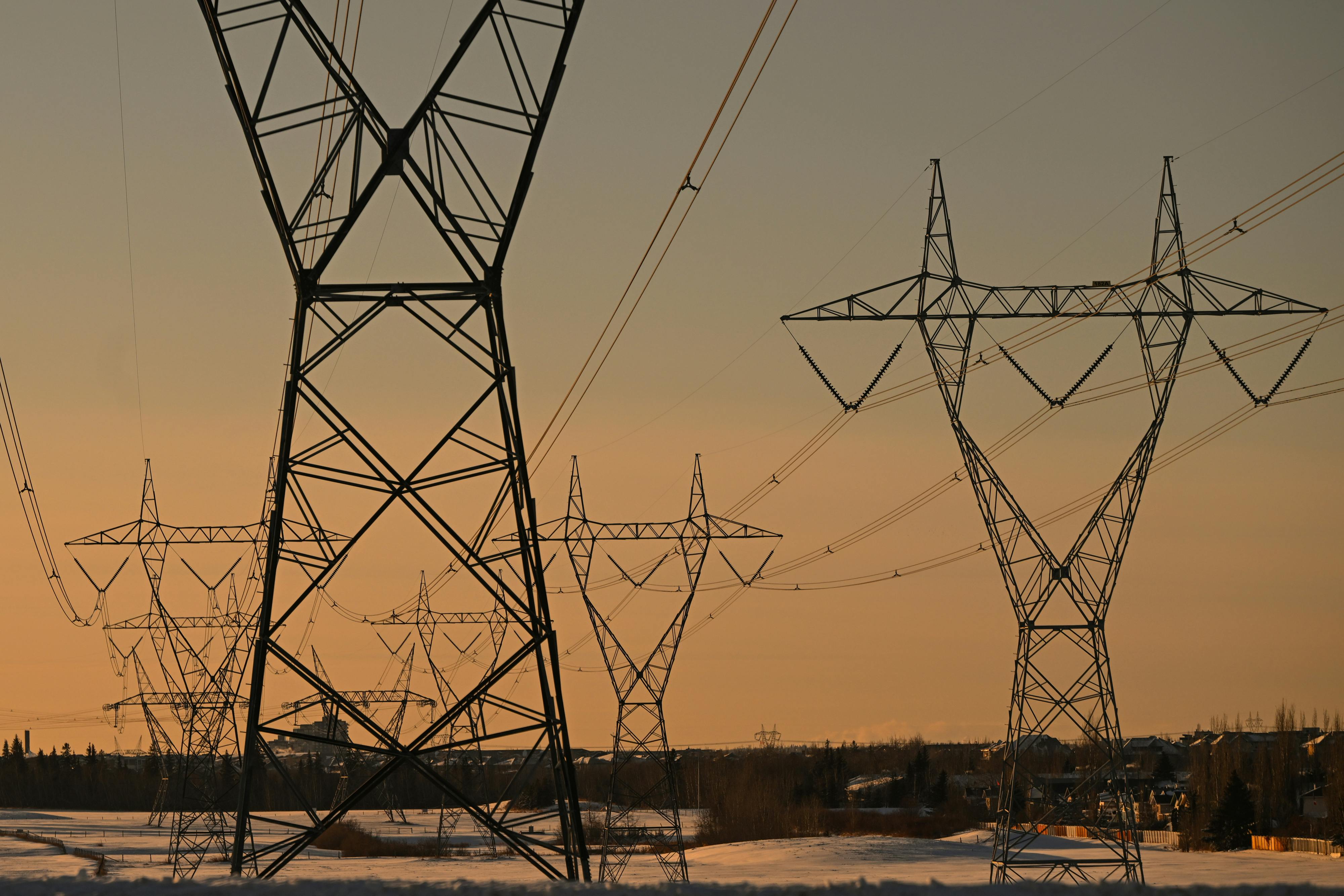 Electrical transmission lines are seen against an orange sky.