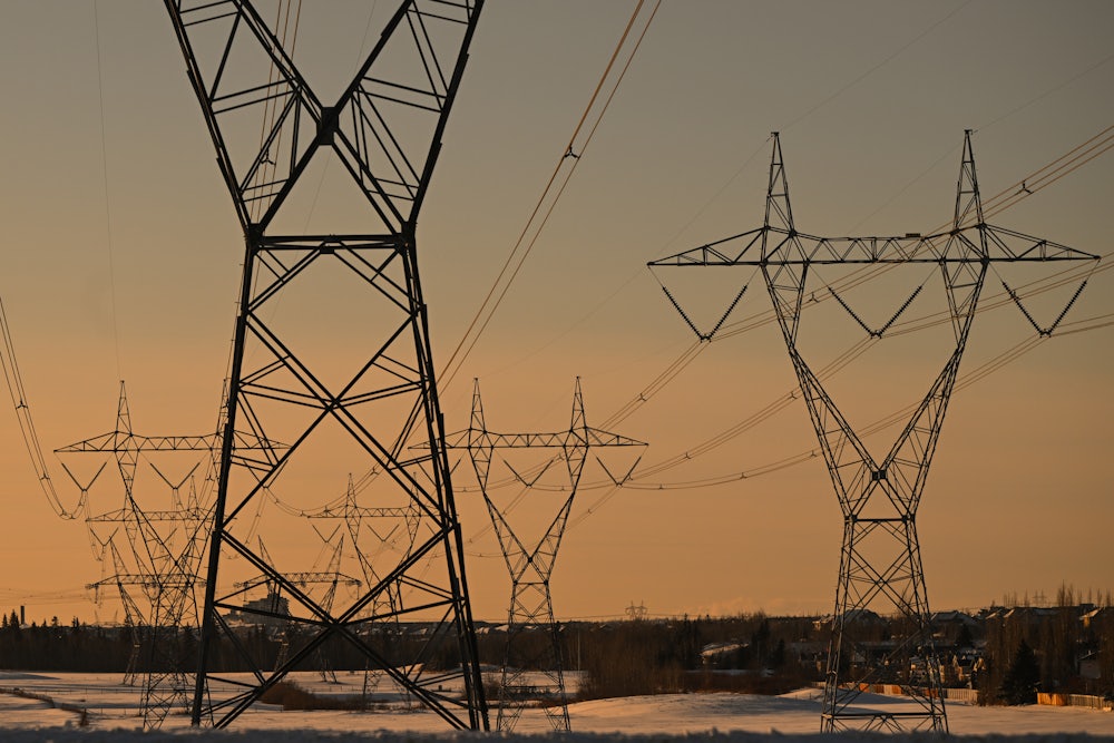 Electrical transmission lines are seen against an orange sky.