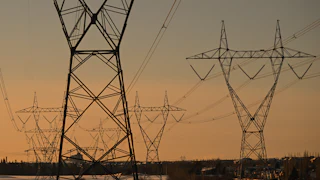 Electrical transmission lines are seen against an orange sky.