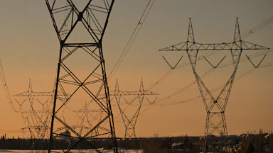 Electrical transmission lines are seen against an orange sky.