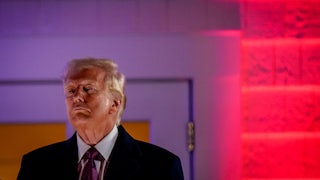 Donald Trump stands in front of a lighted red-purple background
