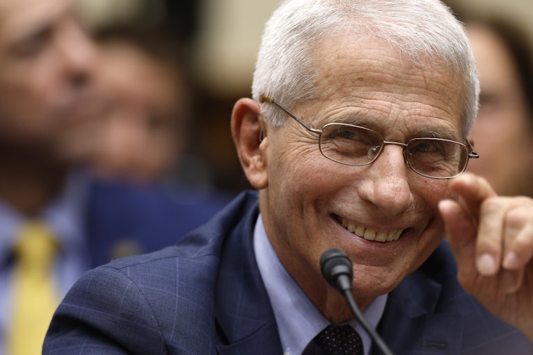 Anthony Fauci smiles as he sits in front of a microphone