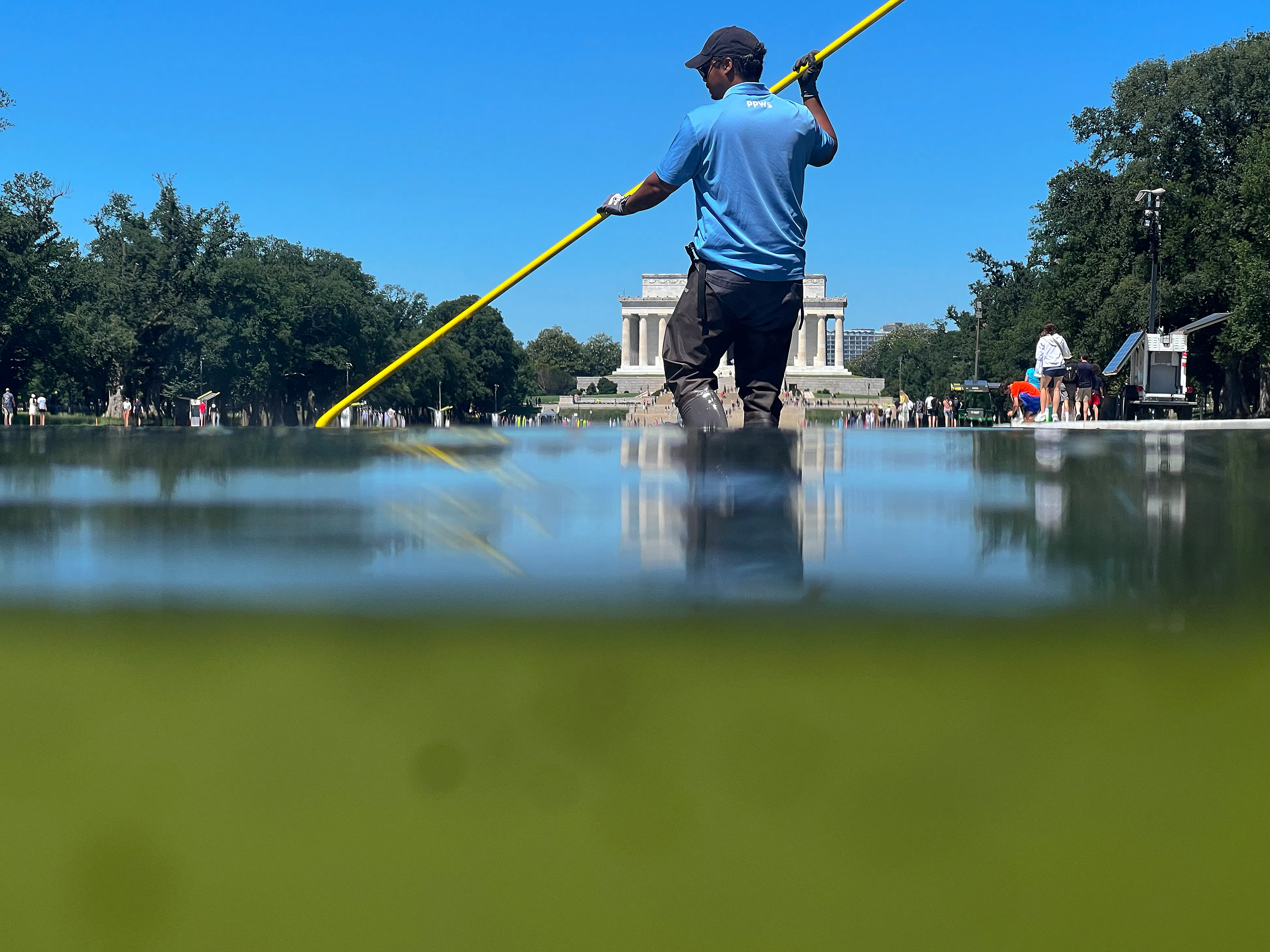 A worker cleans algae out of the Reflecting Pool