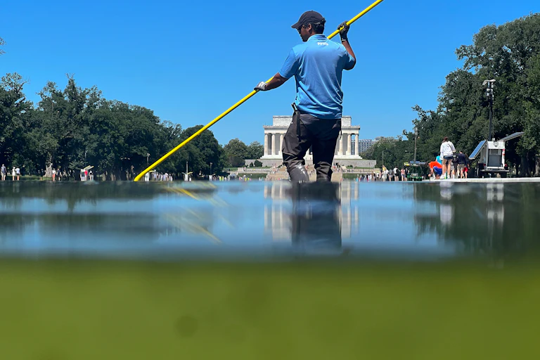 A worker cleans algae out of the Reflecting Pool