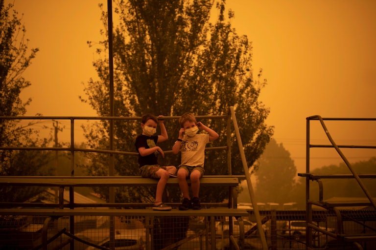 Two children in masks sit on bleachers.
