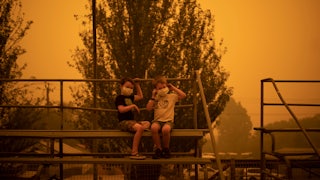 Two children in masks sit on bleachers.