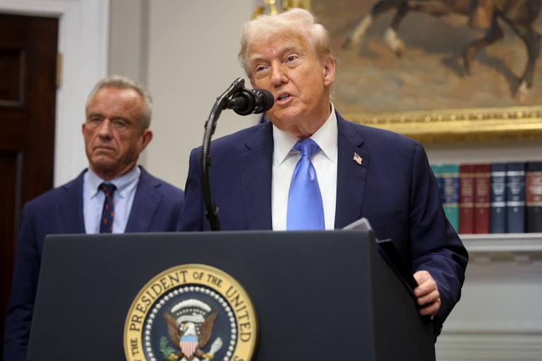 Donald Trump speaks at a podium in the White House. Robert F. Kennedy Jr. stands behind him