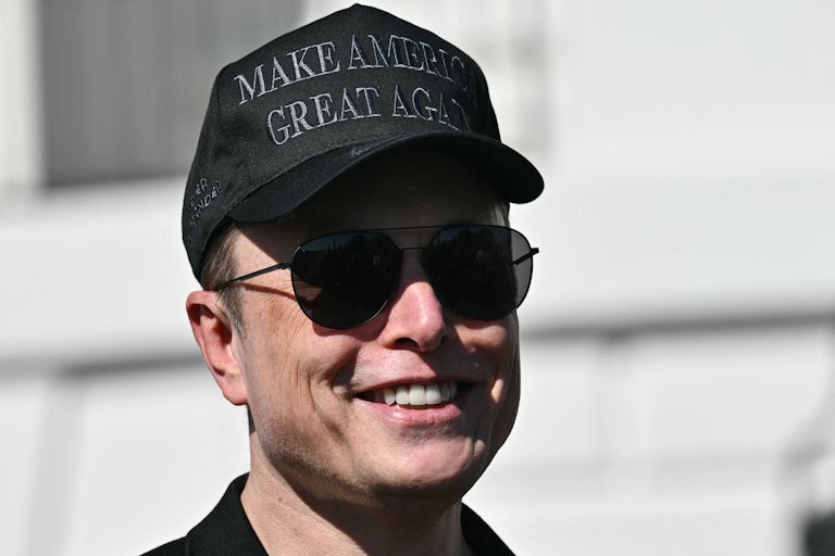 Elon Musk smiles outside the White House wearing sunglasses and a black MAGA cap.