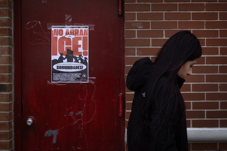 A woman walks in front of a door with a poster warning ICE to stay out of the neighborhood