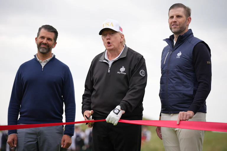 President Donald Trump and his sons Donald Trump Jr. (L) and Eric Trump hold a red ribbon