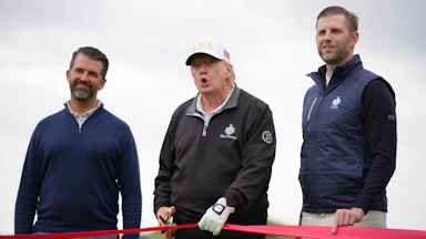 President Donald Trump and his sons Donald Trump Jr. (L) and Eric Trump hold a red ribbon