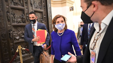 House Speaker Nancy Pelosi walks through the U.S. Capitol, thronged by aides and reporters.