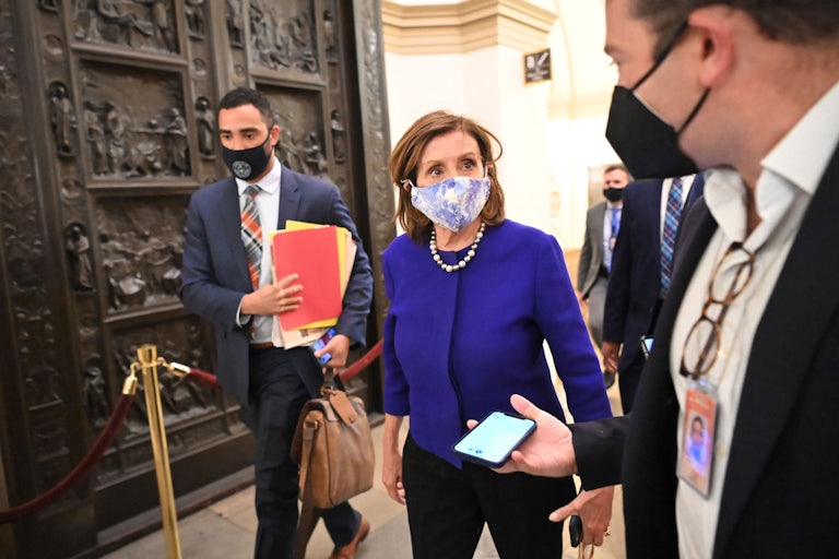 House Speaker Nancy Pelosi walks through the U.S. Capitol, thronged by aides and reporters.