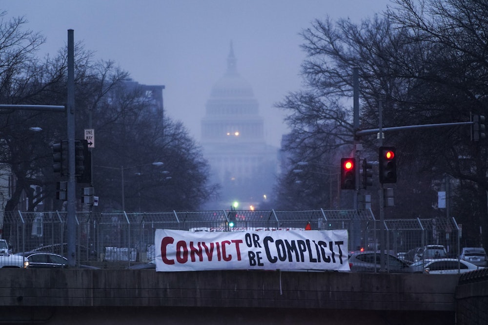 A sign reading "convict or be complicit" hangs from a bridge outside the U.S. Capitol during the impeachment trial.