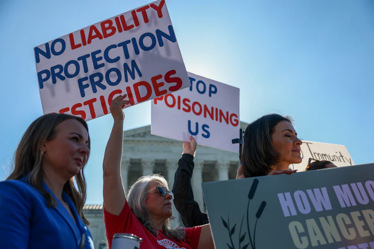 Protesters in front of the Supreme Court hold signs reading "No liability protection from pesticides" and "Stop poisoning us."