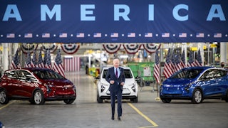President Biden walks in front of red, white, and blue cars.