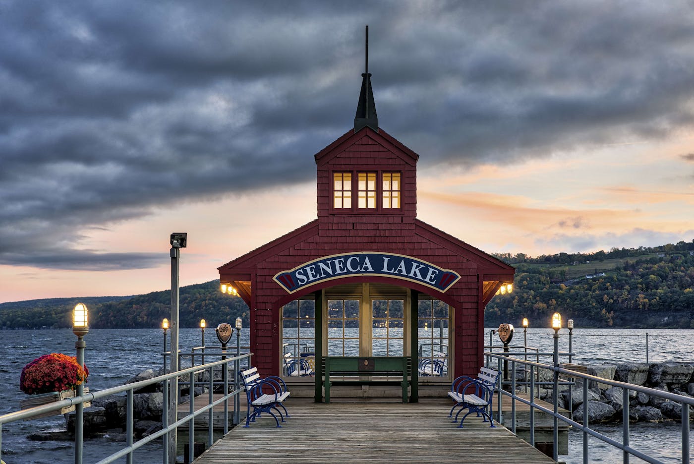 A picturesque structure sits at the end of a dock against a large lake with hills in the background.