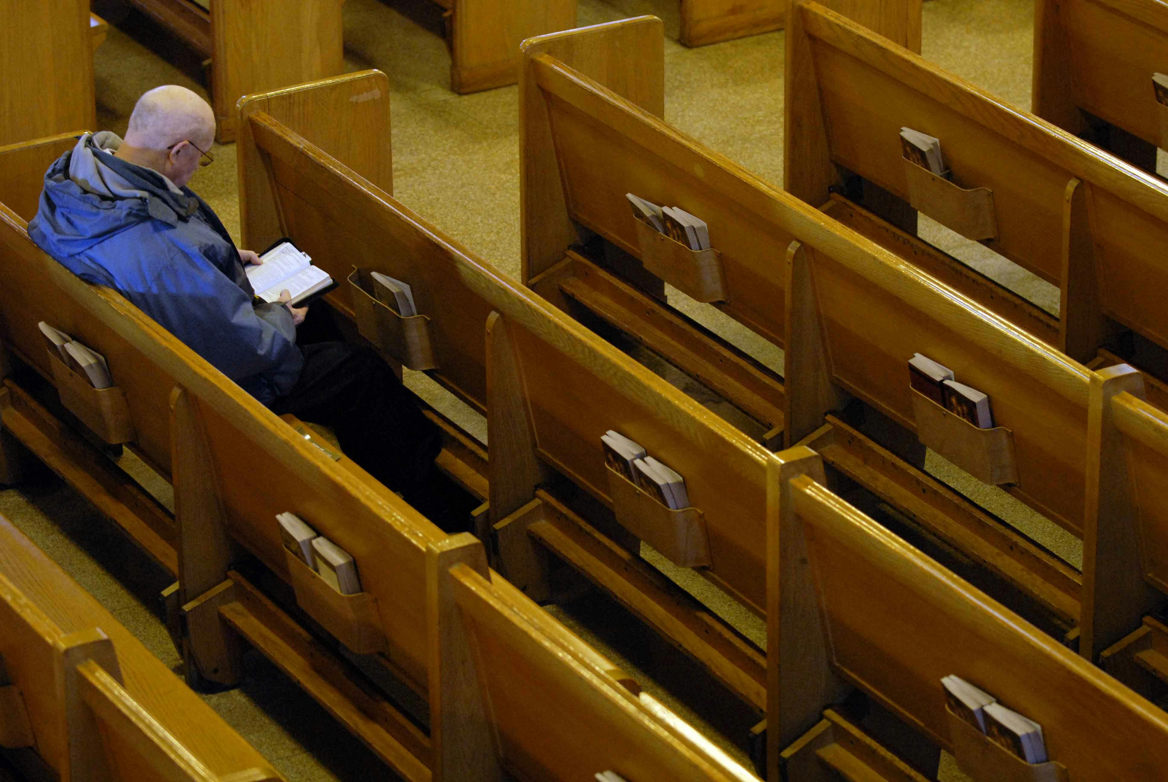 A man reads the bible alone in the pews of an otherwise empty church.