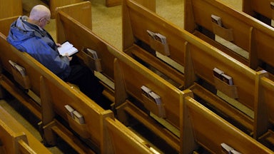 A man reads the bible alone in the pews of an otherwise empty church.