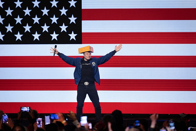 Elon Musk raises his arms while wearing a cheese hat during a rally in Wisconsin