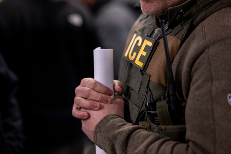 An ICE agent holds a piece of rolled up paper in his hands. His face is not pictured.