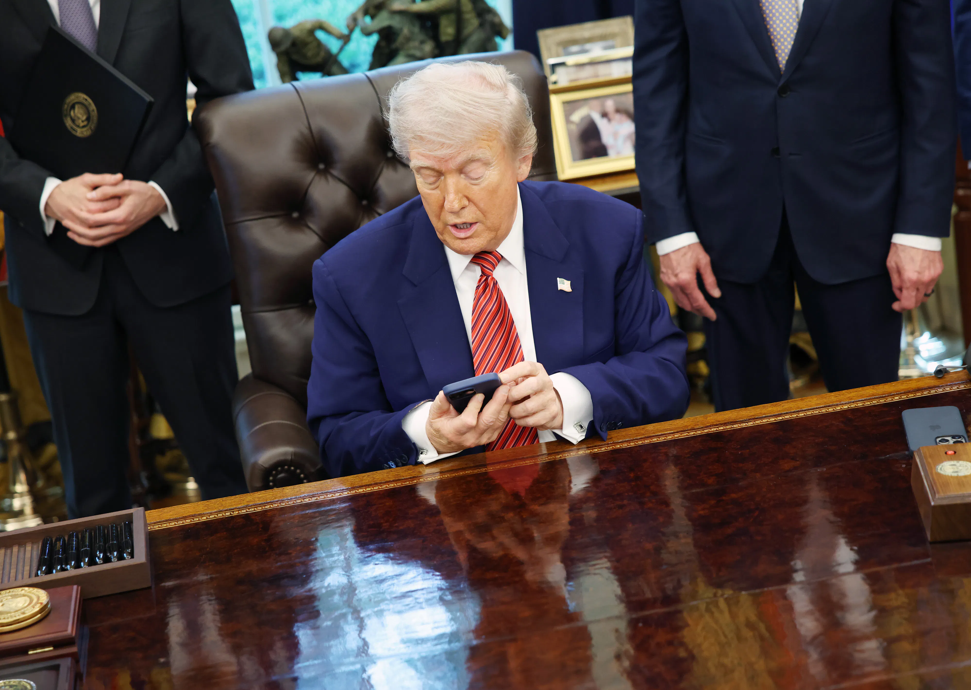 President Donald Trump looks at his phone while sitting in the Oval Office of the White House.