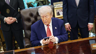 President Donald Trump looks at his phone while sitting in the Oval Office of the White House.