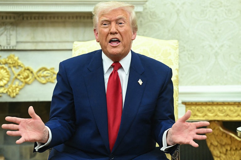 Donald Trump holds his hands out to the side and speaks while sitting in the Oval Office