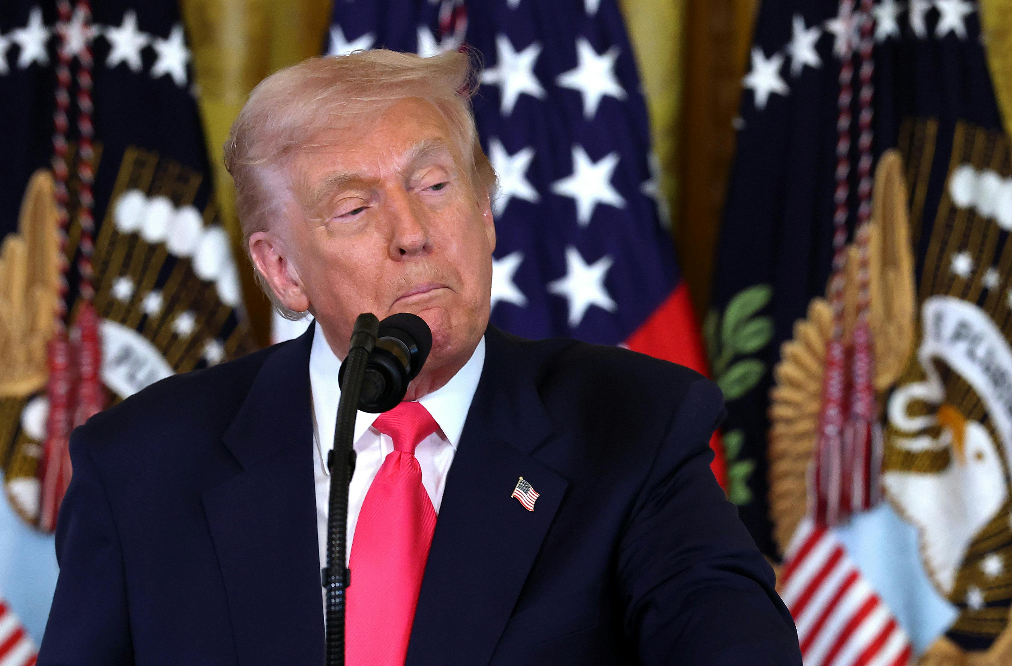 Donald Trump pulls the corners of his mouth down as he stands at a microphone