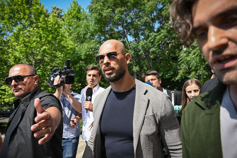 Andrew Tate surrounded by press and one person who appears to be security