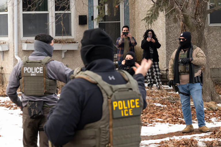 Observers film masked ICE agents outside a suburban home.