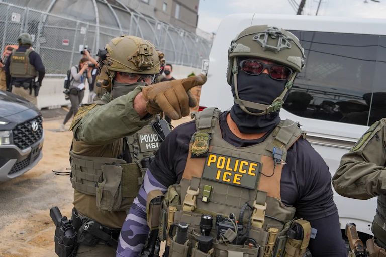 A masked ICE agent points at protesters outside Delaney Hall