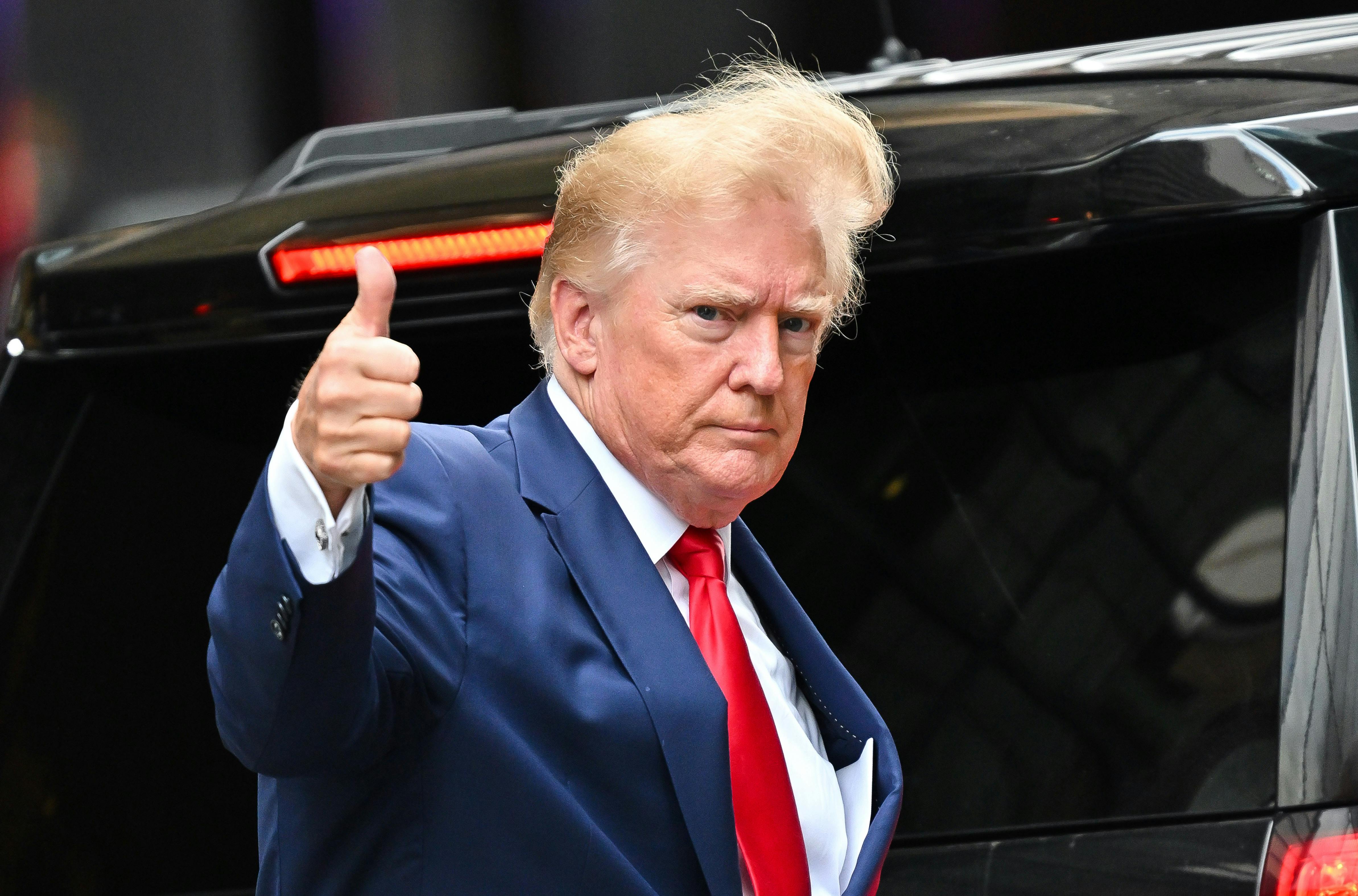 Donald Trump gives a thumbs up with wind blowing his hair.