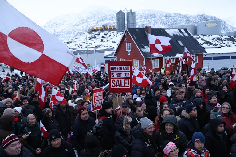 Protesters hold Greenlandic flags and signs that read things like "Greenland Is Not For Sale!"